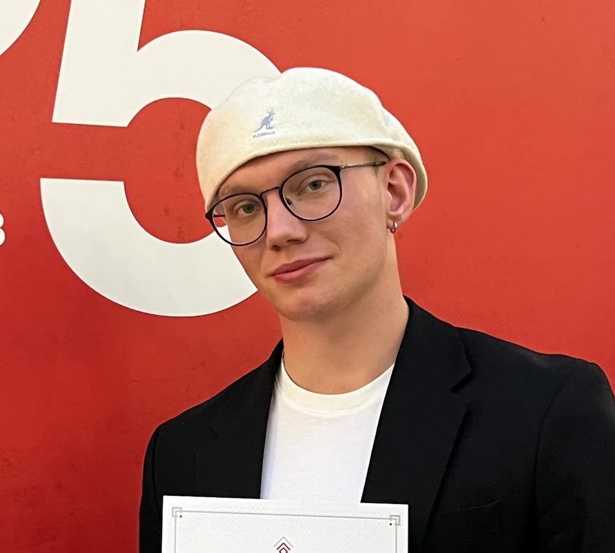 Baldur Logi Gautason in a white beret and glasses, smiling in front of a red wall.
